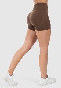 Bruine hoge sportshorts van een gladde, rekbare stof, ontworpen voor comfort en bewegingsvrijheid, gecombineerd met witte sportschoenen.