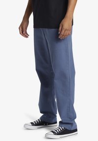 Light blue denim pants with a loose fit, featuring side pockets and contrasting black sneakers with white soles and laces.