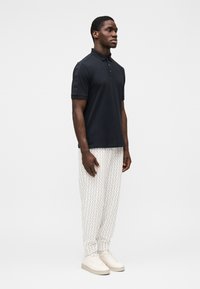 Tumesinine polo särk krae ja kolme nupuga, koos heledate mustriliste pükstega ja valgete tossudega. Sile kangapind.