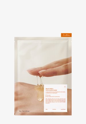 Finger halten transparentes Gel, das auf die Hand tropft, mit der Verpackung der Dr. Althea Vita Glow Maske und der Gebrauchsanleitung sichtbar.