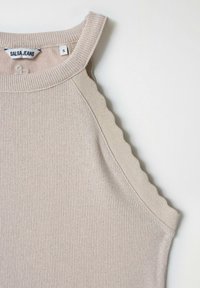 Top sin mangas de color beige con ribetes beige en las hombros en forma de concha. La etiqueta dice "Salsa Jeans," con la talla visible. Textura suave.