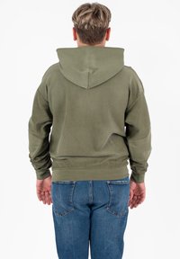 Olijfgroene hoodie met een trekkoordcapuchon, textuurstof en ribgebreide mouwen, gecombineerd met blauwe jeans met opvallende achterzakken.