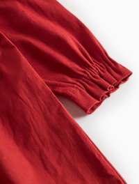 Detaliu al unui articol din bumbac roșu, cu manșete elastice plisate, textură fină și un design fluid, cu un finisaj mat, moale.