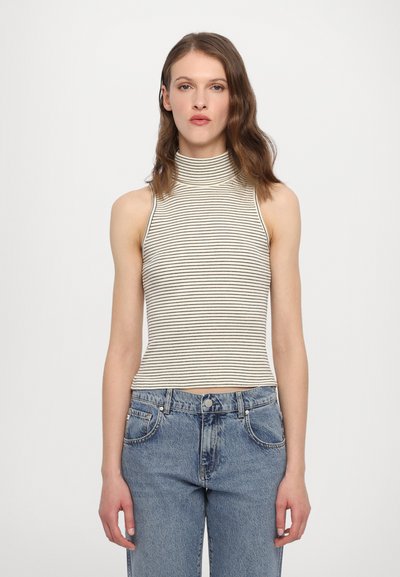 Gestreifter hochgeschlossener Cropped-Top in Creme und Schwarz, aus einem gerippten Material. Kombiniert mit hoch taillierten blauen Jeans.