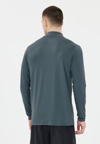 Langärmliges Hemd aus dunkelgrauem Stoff mit glatter Textur und hohem Kragen, mit geradem Schnitt und minimalistischem Design.