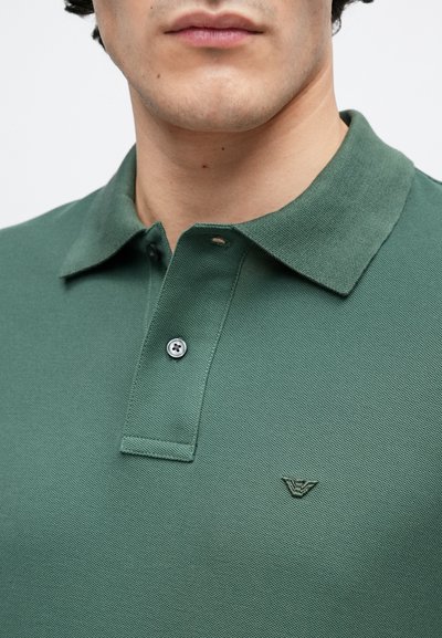 Polo vert en tissu maille texturé, doté d'un col classique, d'une patte à deux boutons et d'un petit logo sur la poitrine.