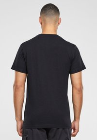 Tricou negru din bumbac cu guler rotund, manșete scurte și un croi lejer. Design simplu fără modele sau ornamentații.