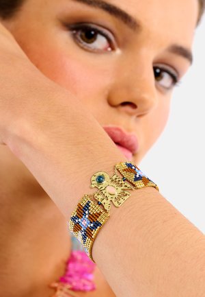 Bracelet en métal avec un travail de perles colorées présentant un motif décoratif de papillon. Comprend des accents bleus et roses avec une finition dorée brillante.