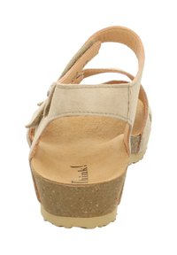 Beige suède sandaal met een kurken plateau, voorzien van een brede band en een hielsteun aan de achterkant. Textuur-inlegzool en verstelbare bandjes.