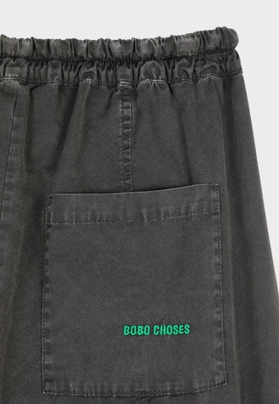 Zwarte katoenen korte broek met een elastische tailleband, voorzien van een achterzak en groene geborduurde tekst "BOBO CHOSES". Soepele textuur, casual ontwerp.