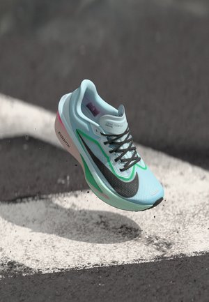 Light blue running shoe with a black mesh upper, green accents, pink sole, and black laces, features “ZOOMX” branding on the side.
