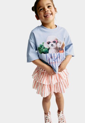 Hellblaues T-Shirt mit einer Grafik eines Hundes mit Sonnenbrille, kombiniert mit einem pink-weiß gestreiften, gestuften Rock. Text lautet „French Riviera Marseille.“