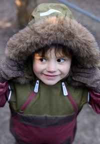 Színes téli dzseki zöld, szőrme szegéllyel ellátott kapucnival, bordó és sötétvörös testtel, valamint barna kötött kesztyűvel. Cipzár és húzófülek láthatóak.