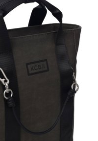 Sac en toile noir et gris avec double poignées, doté d'une fermeture éclair latérale et de finitions en acier inoxydable. Logo "KCB" embossé sur le devant.