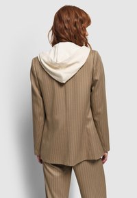 Blazer marrone a righe sottili con un cappuccio crema attaccato sul retro, design strutturato, texture liscia, con maniche lunghe e vestibilità aderente.