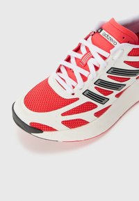 Scarpa atletica rossa con una parte superiore in rete traspirante, dettagli bianchi, pannelli laterali neri e una suola in gomma testurizzata.