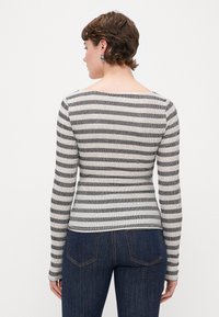 Camiseta de manga larga a rayas en punto acanalado, con rayas en blanco y negro, escote en forma de pala en la parte posterior y silueta ajustada. Combina con jeans de mezclilla oscura.