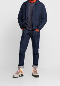 Navy bomber jacket, textured gray sweater with orange accents, dark jeans, and beige hiking boots with orange detail and patterned laces.