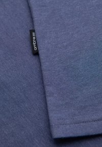 Námořnická modrá tričko vyrobené z měkké, prodyšné tkaniny s hladkým povrchem, s malou černou etiketou s bílým textem na spodním lemě.