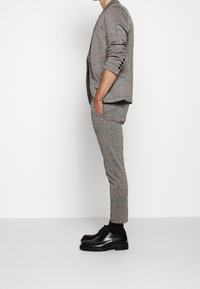 Harmaa ruutukuosisetti punaisilla yksityiskohdilla, sisältäen muotoillun bleiserin ja kapeat housut. Yhdistettynä kiiltonahkaisiin mustiin kenkiin.