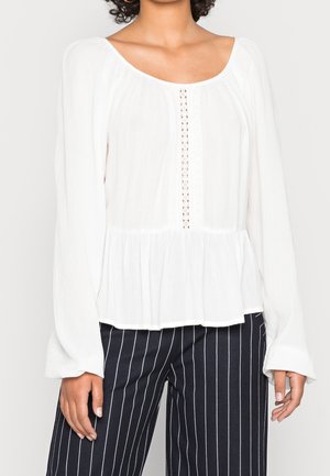 Weiße Bluse mit langen Ärmeln und Peplum-Saum, mit Rundhalsausschnitt, strukturiertem Stoff und einer Reihe kleiner Knöpfe vorne.