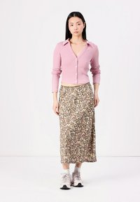Růžový žebrovaný cardigan s knoflíky spárovaný s květinovou maxi sukni. Modelka má na sobě šedé tenisky. Jednoduchý, neformální outfit s kontrastními barvami.