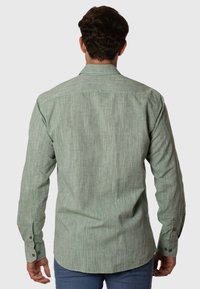 Camisa verde de manga larga, con botones, que presenta una tela texturizada con un sutil patrón a rayas, dobladillo redondeado y puños abotonados.