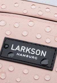 Tessuto impermeabile rosa con gocce in rilievo, dotato di un'etichetta rettangolare nera impresso con "LARKSON HAMBURG" in testo bianco.