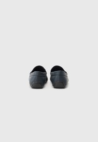 Tamnosmeđi slip-on cipele s glatkom kožnom teksturom, zaobljenim prstima i gumenom potplatom. Stražnji dio ima niski, podstavljeni petu.