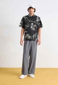 Chemise noire à manches courtes avec des graphiques blancs à thème western ; pantalon gris à jambes larges ; baskets blanches ; casquette blanche avec le logo "Dickies".