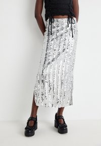 Jupe midi en sequins argentés avec des rayures verticales, une fente sur le côté et une texture lisse. Associée à des chaussures à plateforme noires et épaisses.