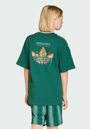 Zelené bavlnené tričko s pixelovanou grafikou na chrbte, zobrazujúcou logá Minecraft a Adidas, spolu so zelenými vzorovanými šortkami.