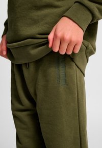 Olivgrüner Hoodie mit gerippten Bündchen und Saum, kombiniert mit passenden Jogginghosen mit dezentem Logodetail und weicher Stoffstruktur.