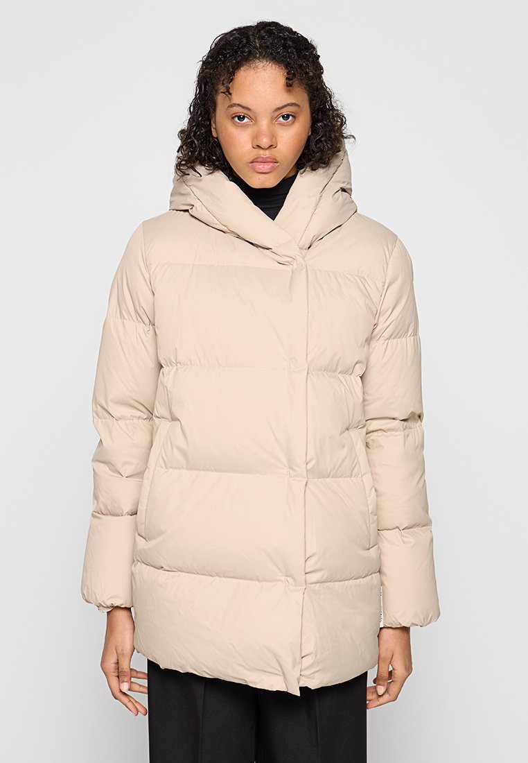 Beżowa kurtka puchowa z pikowanym wzorem, długimi rękawami i dużym kapturem. Gładka tekstura, zapięcie na guziki z przodu i luźny krój.