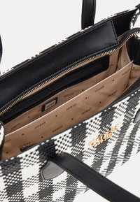 Sac à main à carreaux noir et blanc avec une texture tissée, des accents en cuir, fermeture éclair sur le dessus et un intérieur beige arborant un motif de logo répété.