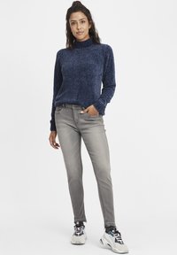 Jersey de cuello alto de punto en color navy con tejido texturizado, combinado con jeans slim-fit grises y zapatillas deportivas multicolores.