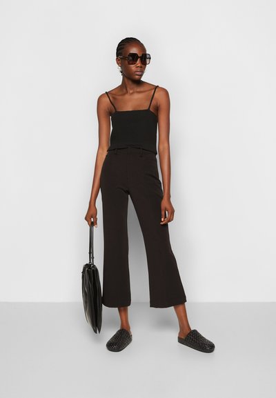 Top de tanque preto canelado, calças pretas flare de cintura alta, sapatos slip-on pretos de trançado, óculos de sol oversized pretos, com uma mala preta.