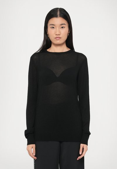 Pull noir à manches longues avec une texture transparente et un col arrondi. Présente une superposition subtile ressemblant à la forme d'un soutien-gorge sur le devant.