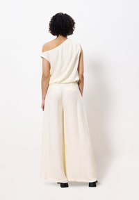 Crèmekleurige wijde broek met een off-shoulder top, gemaakt van lichte stof. Glad textuur, minimalistisch ontwerp, subtiele details aan de achterkant.
