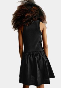 Černé šaty s přiléhavým ribově strukturovaným korzetem a rozšířenou texturovanou sukní s nařaseným pasem, které mají jednotnou černou barvu.