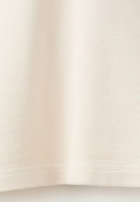 Tissu en coton écru avec une texture tricotée visible et une couture d'ourlet au bord inférieur.