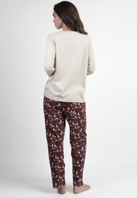 Top de manga larga beige combinado con pantalones burdeos de estampados que presentan diseños de dibujos animados. Tejido suave, corte relajado y diseño hasta el tobillo.