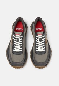 Sneaker in tessuto grigio con lacci bianchi, suola in gomma e accenti rossi sulle sole interne. Presenta un design arrotondato e una superficie testurizzata.