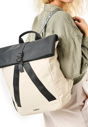 Beige- und schwarze Tasche mit einem umklappbaren Deckel, verstellbarem Riemen und einem glatten Material, das an der Basis ein Logo trägt.