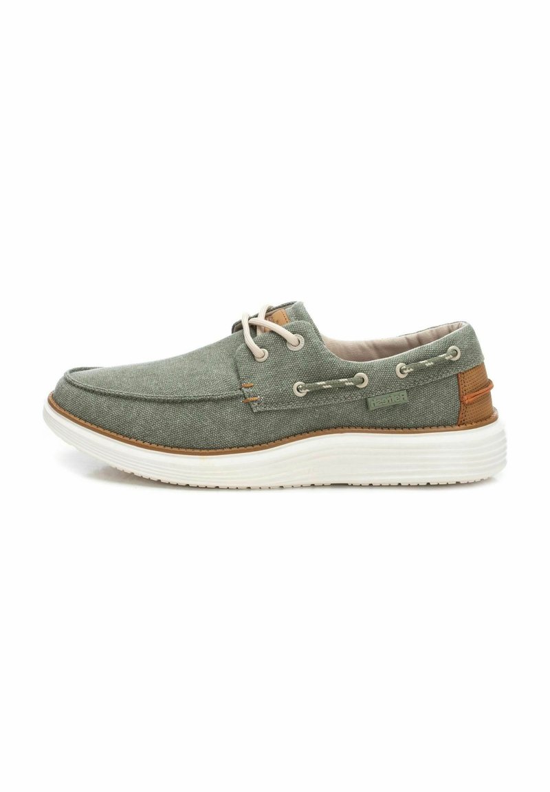 Zapatilla de barco de lona verde con suela de goma blanca, cordones beige y acentos marrones. Presenta detalles cosidos y ojales de metal.