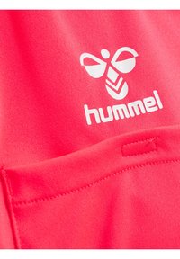 Felroze stof met een gladde textuur heeft een witte Hummel-logo en een klein gestikt zakdetail.