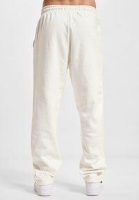 Lyse beige joggerbukser lavet af blødt stof; elastisk talje og sidelommer; løs pasform, der snævrer ind ved anklerne; minimalistisk design.