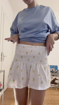 Minissaia branca e texturizada com padrões florais amarelos, cintura elástica e design em camadas. Combinada com uma camisa azul de manga longa.