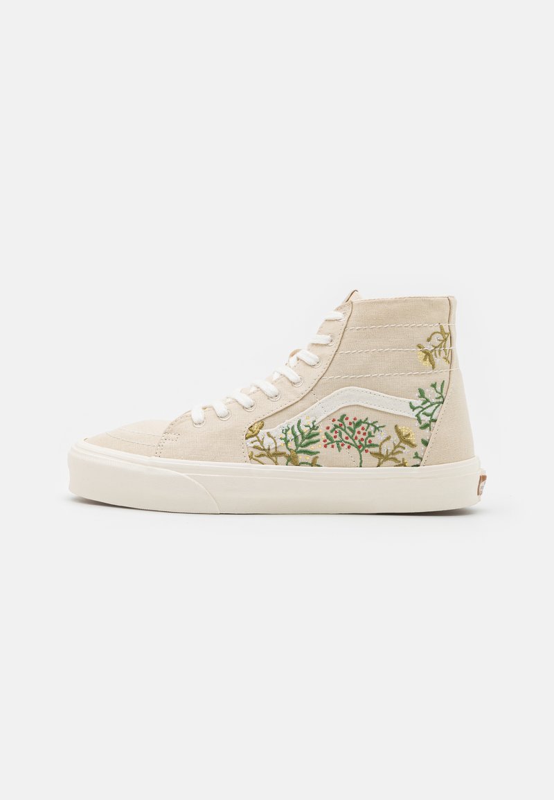 Sapatilhas de cano alto feitas de lona bege com padrões florais bordados em verde e vermelho, apresentando atacadores brancos e uma sola de borracha texturizada.