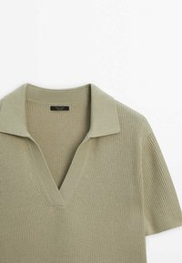 Polo en maille vert olive clair à manches courtes, col en V côtelé et tissu texturé.